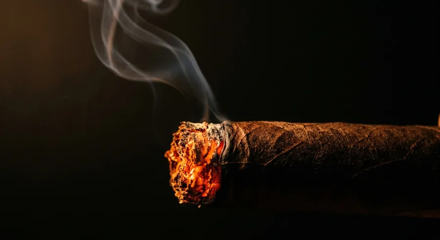 A hand-rolled cigar glowing at the ember, with smoke curling upward