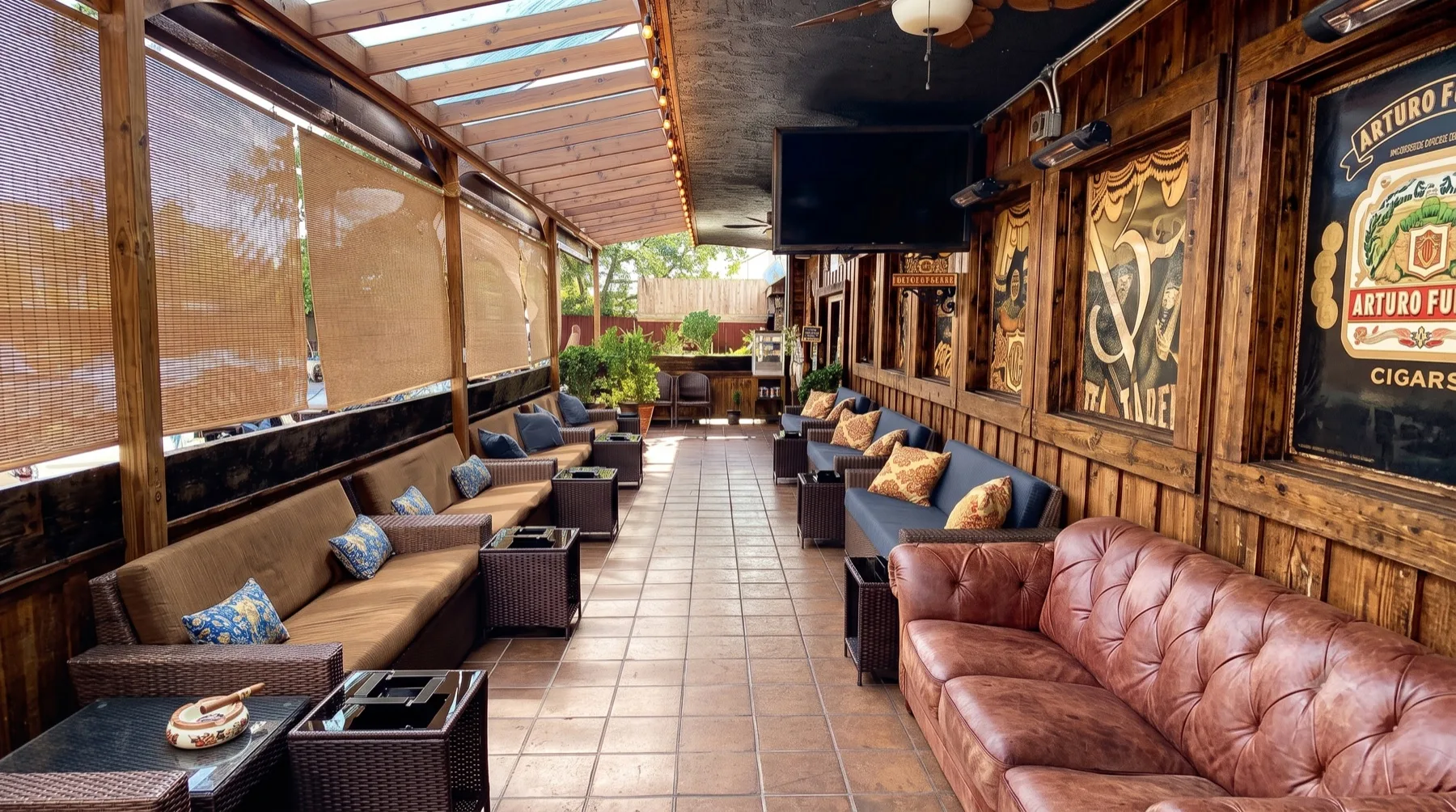 The covered patio lounge at Lord Puffer Cigars, with wood paneling, string lights, leather and wicker seating, and Arturo Fuente artwork on the wall